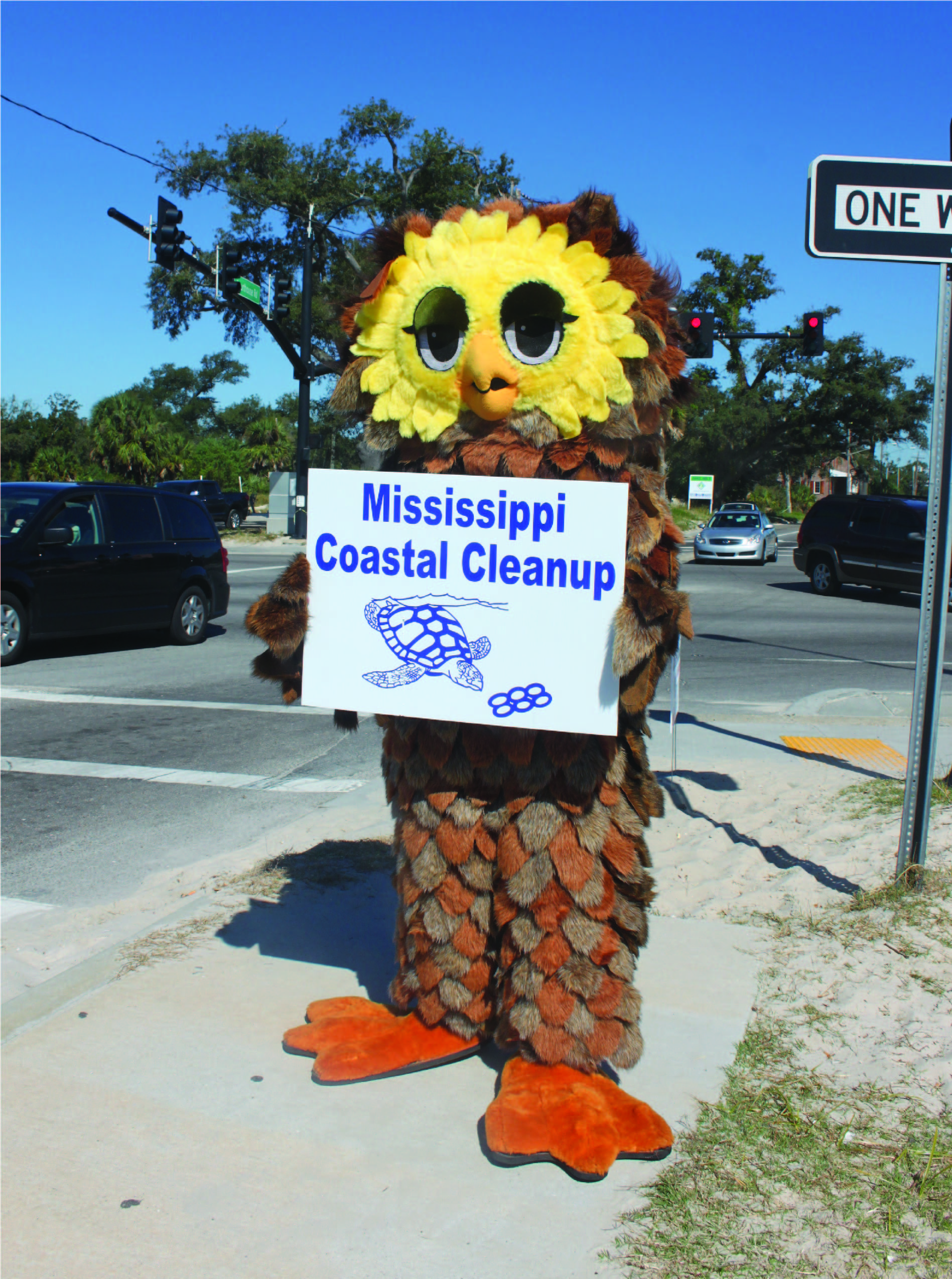 person in an owl costume holding a coastal cleanup sign